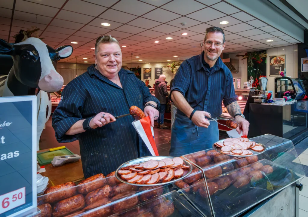 Vriendelijke slagers bieden Grillworst aan in een slagerij. Worst proeven. slager in Spijkenisse