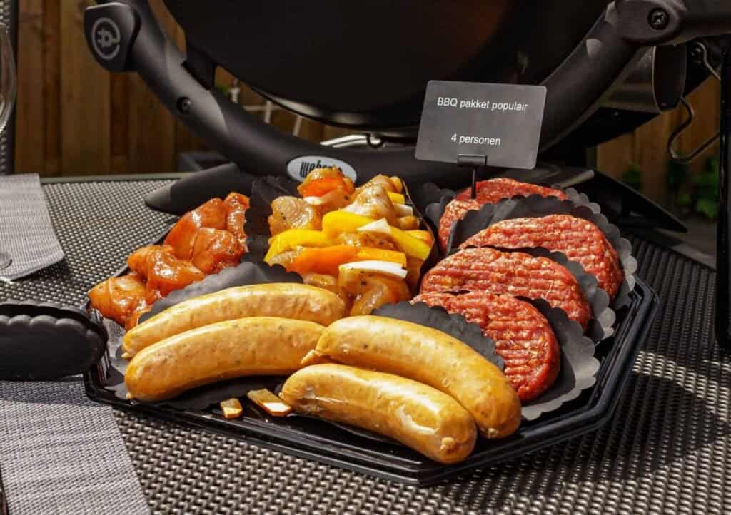 BBQ pakket - Worsten, hamburgers, shaslicks en gemarineerd vlees op een zwarte schaal opgemaakt door Keurslagerij van den Akker uit Spijkenisse